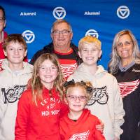 Large family dressed in Red Wings jerseys and sweatshirts posing for photo in front of GVSU backdrop